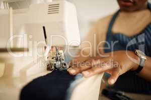 Closeup of hands of tailor using sewing machine. Fashion designer feeding denim through sewing machine. Hand of a seamstress stitching a piece of material. Creative businesswoman working in a studio