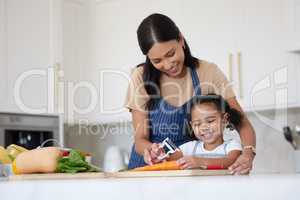 Caring mother and adorable daughter cooking and bonding at home. Happy little girl helping her mother while using peeler and preparing vegetables for a healthy meal together