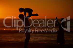 A young family silhouetted on the beach while playing together. Cheerful family with one child, two parents and daughter having fun during sunset at the beach