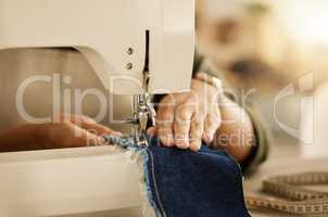 Closeup of the hand of a seamstress using a sewing machine. Fashion designer sewing denim fabric on a machine. Tailor using a sewing machine. Creative entrepreneur stitching a piece of material