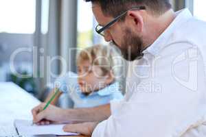 Young homeschool little boy sitting with his father at the kitchen table. Caucasian male single parent checking his sons homework and grading his paper at the kitchen table in a bright room