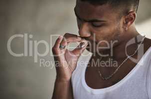 Getting high just to get by. a young man smoking a marijuana cigarette against an urban background.