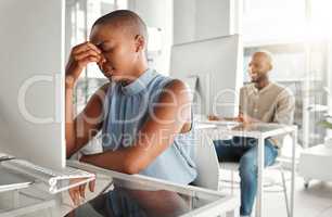 Young stressed african american businesswoman suffering from a headache while working on a desktop computer at work. One unhappy black female businessperson suffering from anxiety while working on a computer at a desk in an office