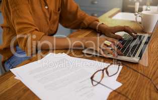 Mixed race businesswoman typing en email on a laptop while working from home. One hispanic female businessperson working on a laptop alone at home