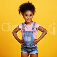 Studio portrait mixed race girl looking standing with her hands on her hips isolated against a yellow background. Cute hispanic child posing inside. Happy and cute kid smiling and looking confident