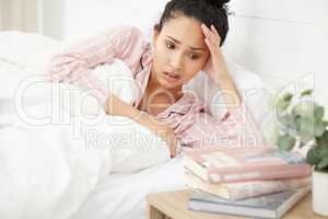 Id rather go back to sleep than study. Shot of a young woman looking stressed while looking at books on her bedside table.