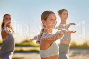 Diverse smiling yoga women in warrior pose during outdoor practice in remote nature. Group of happy active friends bonding and balancing while stretching at sunset. Beautiful young active zen people