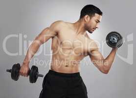 Abs of steel takes hours of dedication. Studio shot of a young man practicing his bicep curls against a grey background.