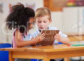 Learning with a little help in the classroom. Shot of two preschool students looking at something on a digital tablet together.
