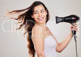 Im going to blow them away. Shot of a beautiful young woman blowdrying her hair while standing against a grey background.