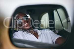 One African American man looking in the car mirror while taking a roadtrip. Smiling black man enjoying the weekend and taking a trip in a vehicle while wearing sunglasses