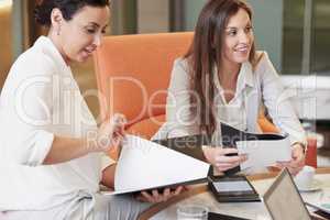 Two business women with laptops and notepads having a meeting in their office. Two business women with laptops and notepads having a meeting in their office.
