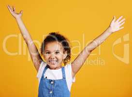 Studio portrait mixed race girl showing surprise with her hands raised isolated against a yellow background. Cute hispanic child posing inside. Happy and carefree kid lifting her hands upwards
