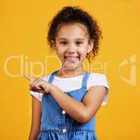 Studio portrait mixed race girl pointing sideways towards copyspace isolated against a yellow background. Cute hispanic child posing inside. Happy and cute kid showing or endorsing company or product