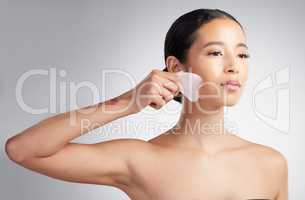 A beautiful mixed race woman using a rose quartz gua sha for deep penetration cell renewal. Young hispanic woman using anti ageing tool against grey copyspace background