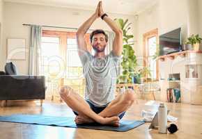 One young caucasian man sitting with legs crossed and eyes closed meditating in harmony with hands together in namaste gesture while practising yoga at home. Calm, relaxed and focused guy feeling zen while praying quietly for stress relief and peace