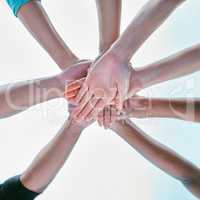 Closeup of diverse group of people from below stacking hands together in a pile to express unity, support and trust. Multiracial community huddled in a circle to celebrate winning achievement. Joining for collaboration and team spirit