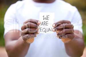 Equal pay isnt just a womens issue. Shot of a unrecognizable man holding a card in protest in a park.