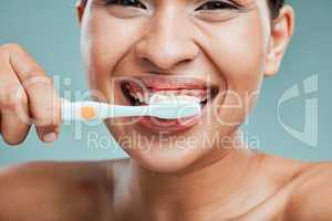Studio portrait of an attractive young woman brushing her teeth against a green background.Latin female taking care of her dental hygiene and oral health