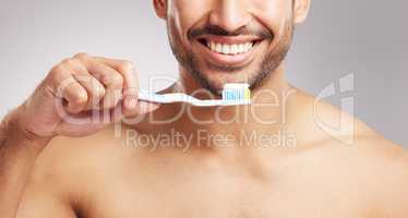 Closeup young mixed race man shirtless in studio isolated against a grey background. Hispanic male brushing his teeth. Taking caring of mouth and oral hygiene to promote dental health and healthy gums