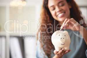 One happy young mixed race woman holding a piggybank and depositing a coin as savings. Hispanic woman budgeting her finances and investing money into her future. Saving funds for financial freedom