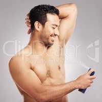 Handsome young mixed race man shirtless in studio isolated against a grey background. Hispanic male applying deodorant to his underarms. Healthy and fresh, making sure to look and smell clean