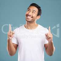 Handsome young mixed race man pointing towards copyspace while standing in studio isolated against a blue background. Happy hispanic male advertising or endorsing your product, company or idea