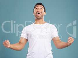 Handsome young mixed race man celebrating victory or success while standing in studio isolated against a blue background. Hispanic male cheering and pumping his fists at success or achievement