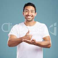 Handsome young mixed race man giving thumbs up while standing in studio isolated against a blue background. Hispanic male showing support or appreciation. Backing or endorsing a product or company