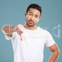 Handsome young mixed race man giving thumbs down while standing in studio isolated against a blue background. Hispanic male showing disapproval or rejection. Feeling unimpressed, bad or negative