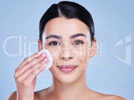Studio Portrait of a beautiful mixed race woman using a cotton pad to remove makeup during a selfcare grooming routine. Hispanic woman applying cleanser to her face against blue copyspace background