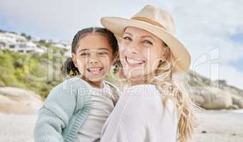 Portrait of a mature mother and her biracial innocent little daughter smiling and standing on the beach smiling. A happy woman and her adopted girl bonding on a day out during a summer vacation