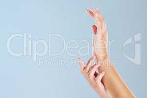 Closeup of a womans hands with a blue studio background and copyspace. Zoom in on manicured fingernails touching soft skin after using a beauty treatment or skin mask. Hand model with copy space