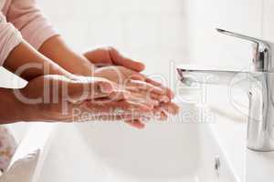 An unknown mixed race father and daughter washing their hands together in a bathroom at home. Unrecognizable single African American parent teaching his daughter about hygiene