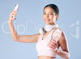 Mixed race fitness woman posing with her phone in studio against a blue background. Young hispanic female athlete taking selfie pictures with her smartphone to track her personal fitness growth