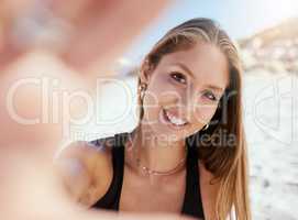 One beautiful young caucasian woman relaxing and taking a selfie photograph while sitting on the beach. Enjoying a summer vacation or holiday outdoors. Taking time off and getting away from it all