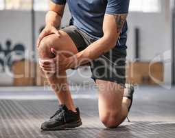 Closeup of one caucasian man holding his sore knee while exercising in a gym. Male athlete suffering with painful leg injury from fractured joint and inflamed muscles during workout. Struggling with stiff body cramps causing discomfort and strain