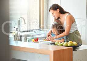 Loving mother and small daughter chopping vegetables and preparing a salad in the kitchen at home. Girl bonding with mother while learning to cook