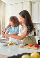 Happy mother teaching little daughter to cook in kitchen at home. Little girl adding seasoning pepper grinder to a bowl while making a salad with mom