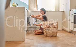 Young hispanic mother and her daughter sorting dirty laundry in the washing machine at home. Adorable little girl and her mother doing chores together at home