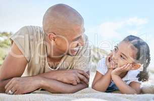 Smiling single father and little daughter looking at each other while relaxing on a beach. Adorable girl bonding with her dad and enjoying vacation. Man and child having fun and enjoying family time