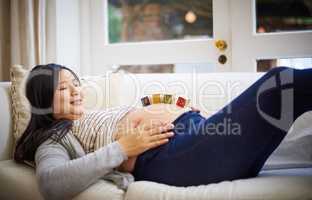Having a positively relaxing pregnancy. an attractive young pregnant woman balancing wooden blocks on her tummy while relaxing on the sofa at home.