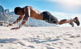 Fit young black man doing plank hold exercises on sand at the beach in the morning. African American muscular male bodybuilder athlete doing bodyweight workout to build a strong core and endurance