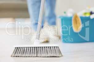 An unrecognizable woman cleaning the floor of her apartment. One unknown woman using a broom to clean the floor of dust