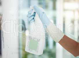 One unrecognizable woman holding a cleaning product while cleaning her apartment. An unknown domestic cleaner wearing latex cleaning gloves