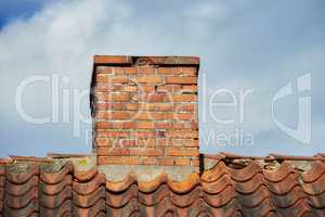 An orange bricked roof with chimney against the blue sky with copy space on a sunny day. A brick chimney on the roof in the blue cloudy sky background. A closeup of the chimney on the rooftop.