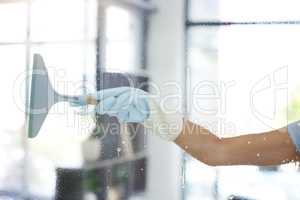 One unknown mixed race domestic worker using a squeegee on a window. An unrecognizable woman enjoying doing chores in her apartment