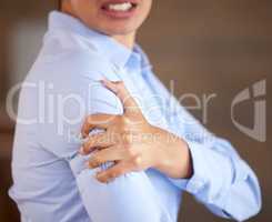 Closeup of unknown mixed race businesswoman standing alone and suffering from sore shoulder or arm while working in an office. Hispanic professional in pain while holding an injury. Injured on the job