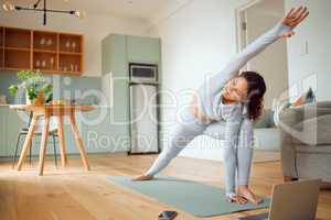 Beautiful young mixed race woman using a laptop to follow an online class while practicing yoga at home. Hispanic female exercising her body and mind, finding inner peace, balance and clarity