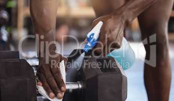 Closeup of unknown african american athlete using spray bottle to sanitise dumbbell weights in gym. Active black man cleaning equipment in hygiene routine to protect and prevent covid through exercise